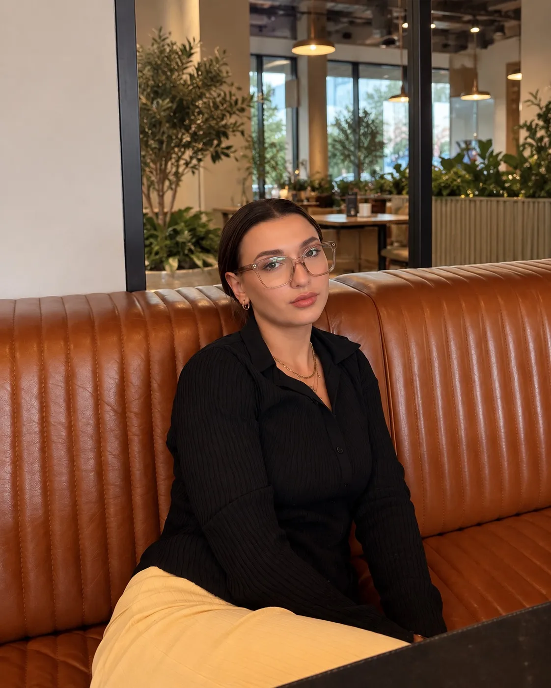 Aleksandra Walichrad w okularach i czarnej koszuli, siedząca na skórzanej kanapie w kawiarni